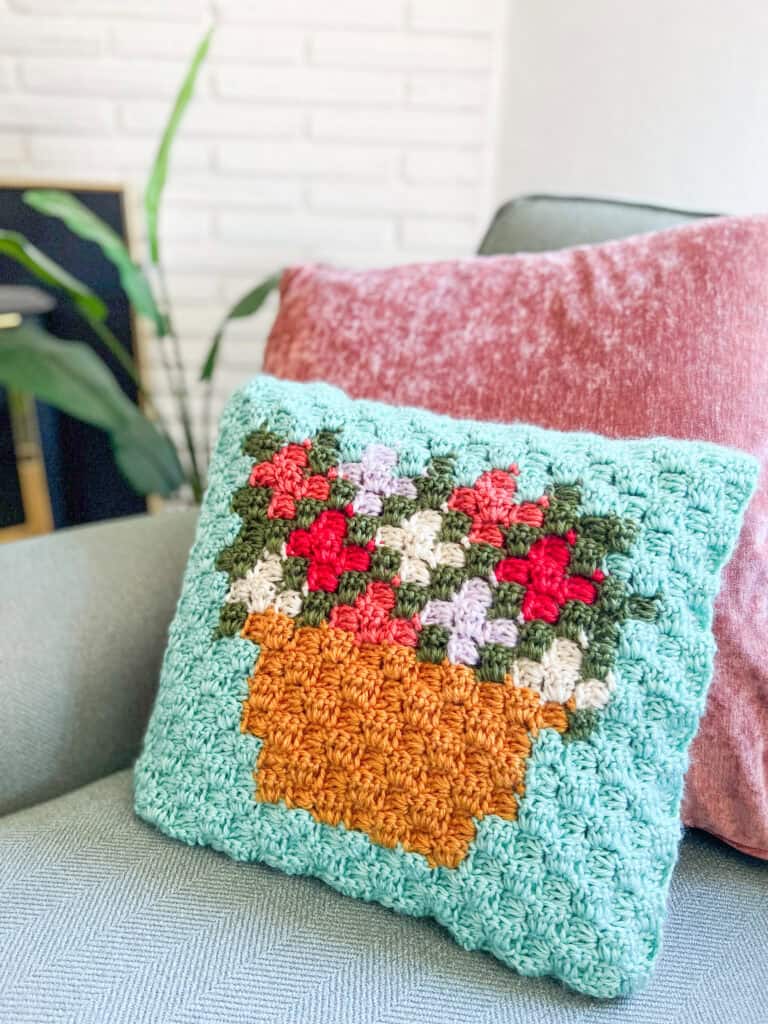 Themed pillow with colorful flowers in a pot, perfect for plant lovers.