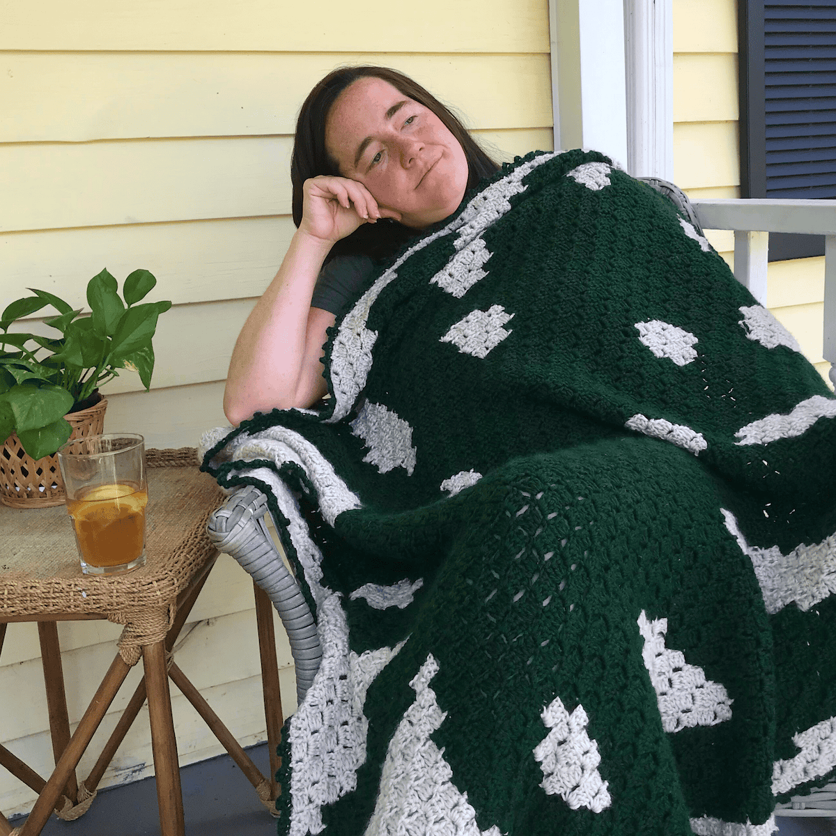 Woman relaxing with a black and white crochet blanket on porch.