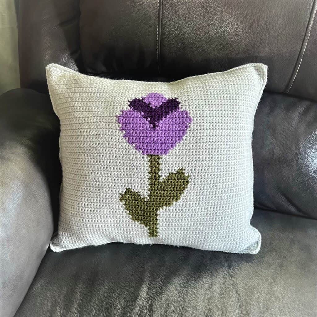 Cross-stitched purple flower pillow on white background, decorative home accent.