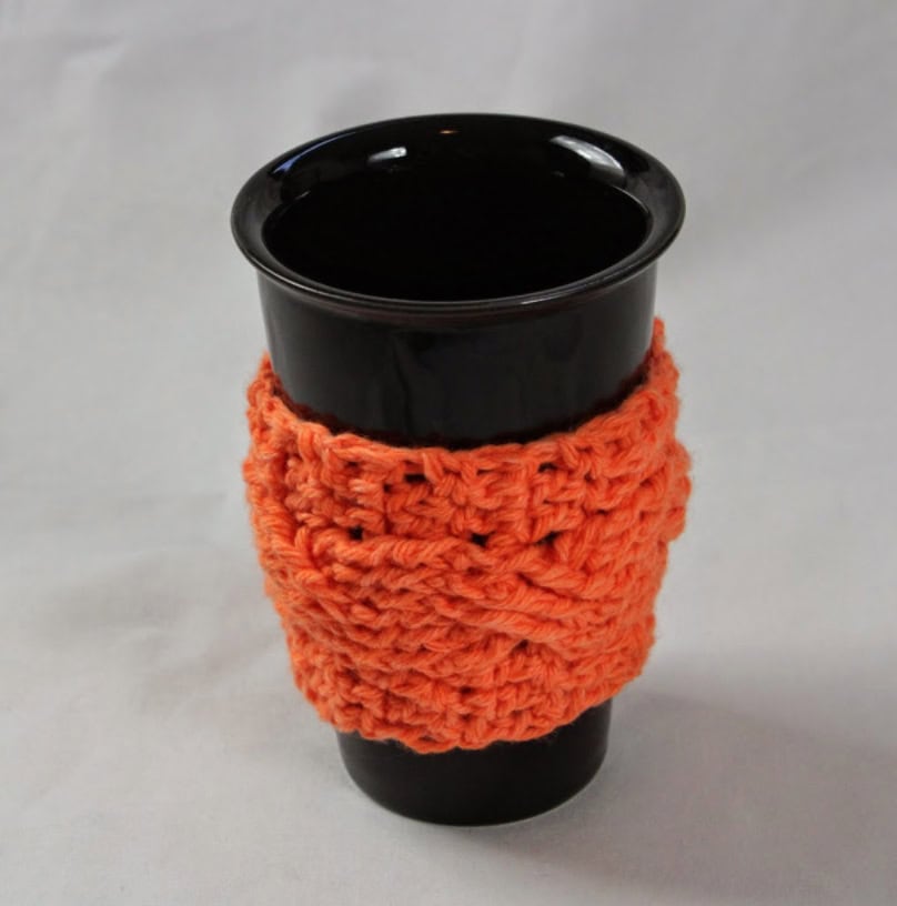 Crochet coffee mug cozy in bright orange, perfect for protecting surfaces and adding style.