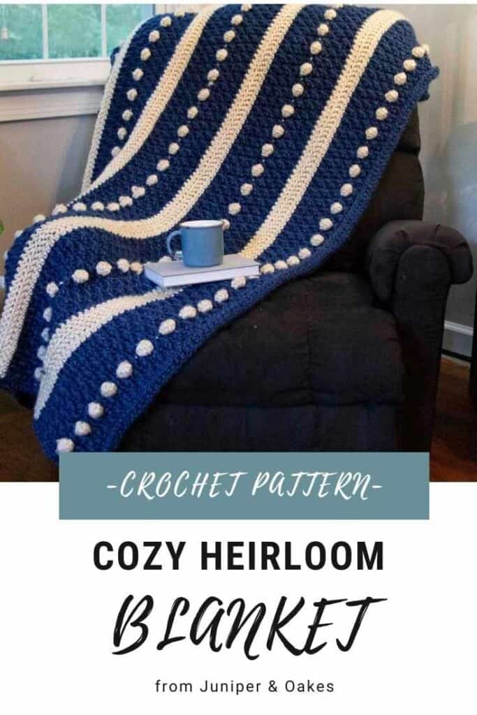 Crochet heirloom blanket with blue and white stripes and pom-pom accents.