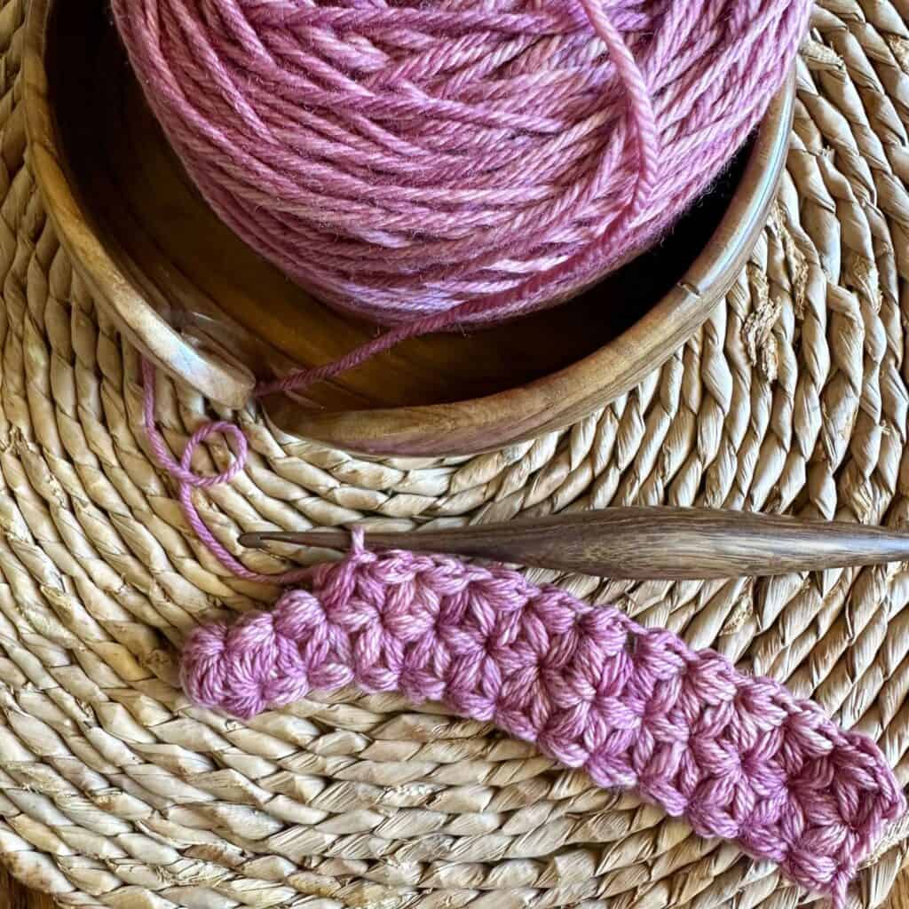 Yarn and crochet hook for knitting or crochet projects on a textured woven background.