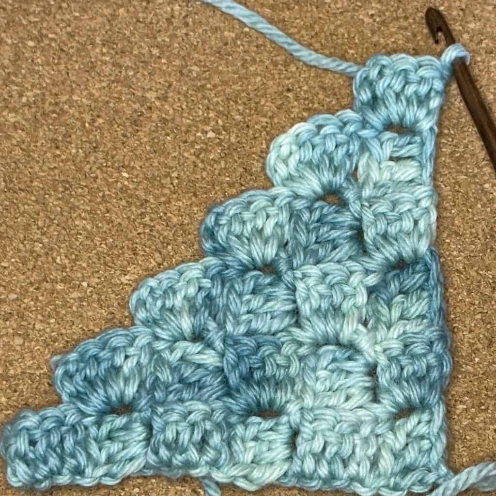 Hand-crocheted blue yarn piece with textured pattern on a cork surface.