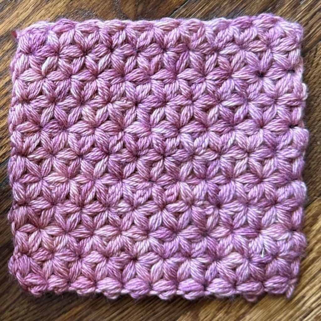 Lavender crocheted square with textured stitch pattern on wooden surface.