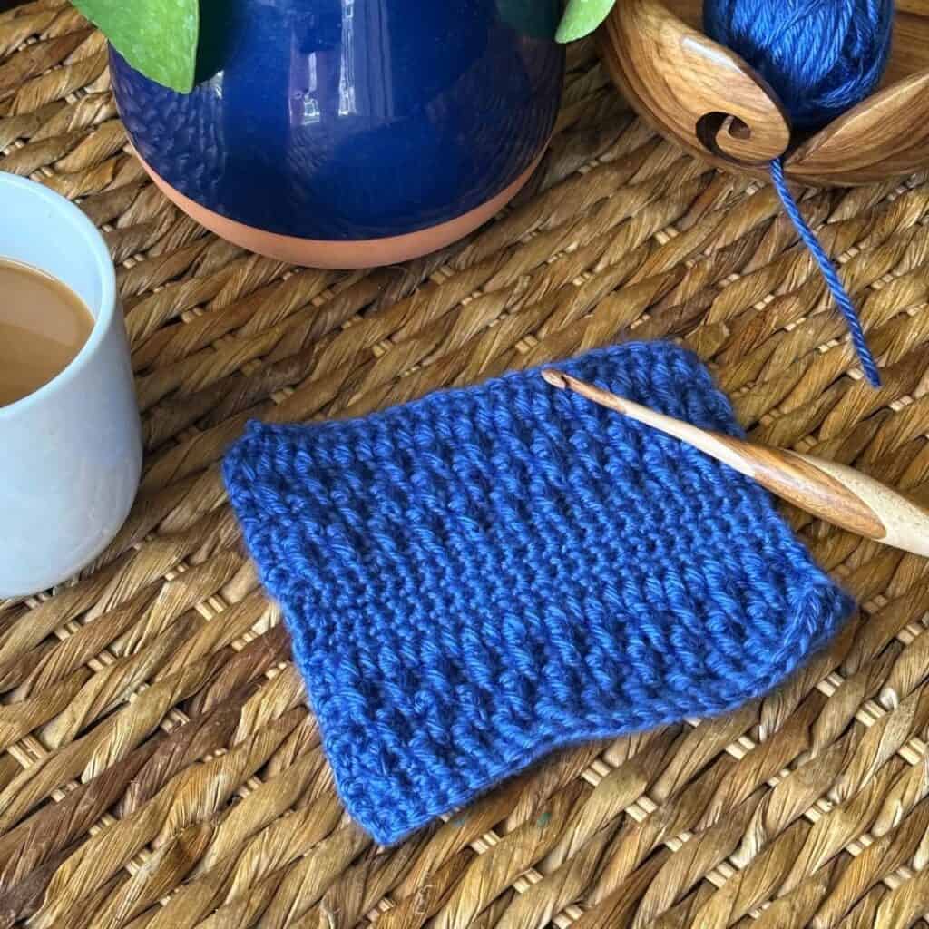 Blue knitted swatch with a wooden knitting needle on a woven surface.