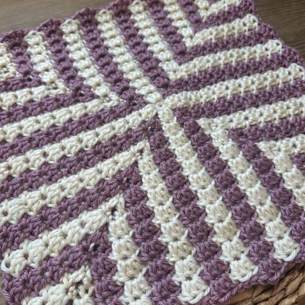Close-up of a colorful mosaic granny square crochet pattern in purple and cream.