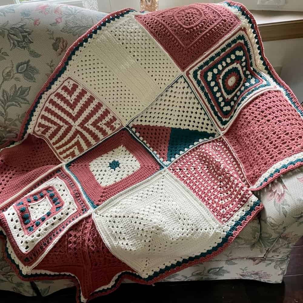 Crochet blanket featuring vibrant, multicolored squares and intricate patterns, draped over a floral.