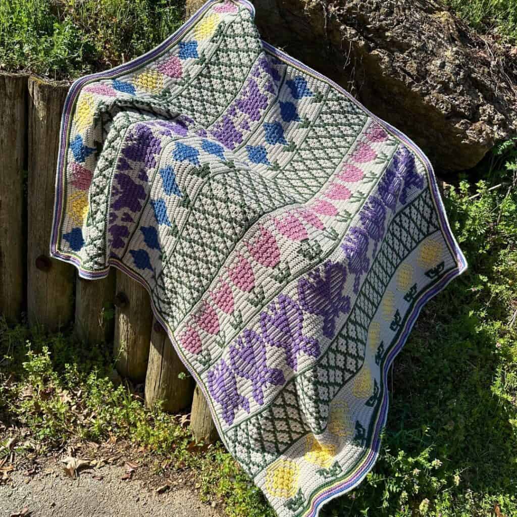 A springtime mosaic crochet blanket featuring pastel colors with images of flowers and butterflies.