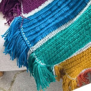 Crochet blanket featuring colorful stripes and a decorative fringe border, perfect for cozy home dec.
