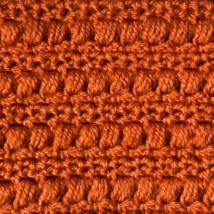 Up of a vibrant orange crochet fabric showcasing the puff and mesh stitch pattern.