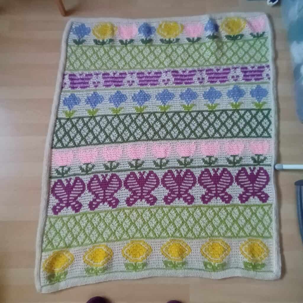 Knitted floral rug with colorful patterns and flowers in pink, yellow, purple, and green.