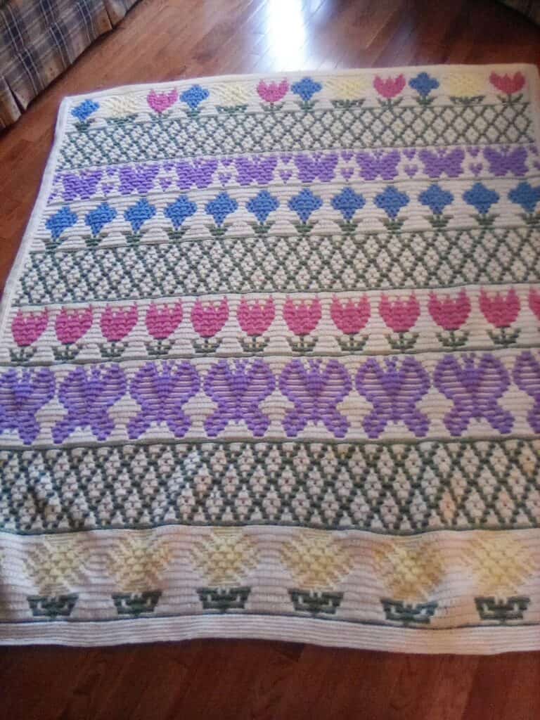 Handcrafted woven textile featuring floral and geometric patterns in pink, purple, and green.