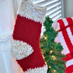 Red and white faux fur crochet Christmas stocking hanging by a window.