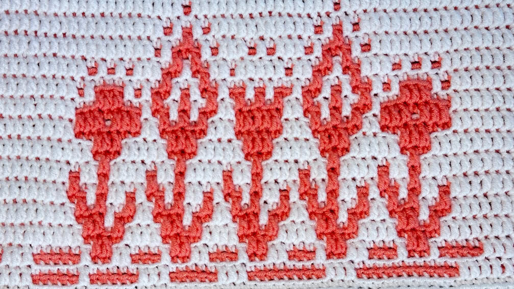 Close-up of a colorful crochet mosaic blanket strip with summery flowers in coral and white.