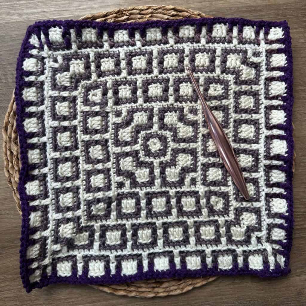 Mosaic crochet square with white and purple yarn, featuring intricate geometric design.