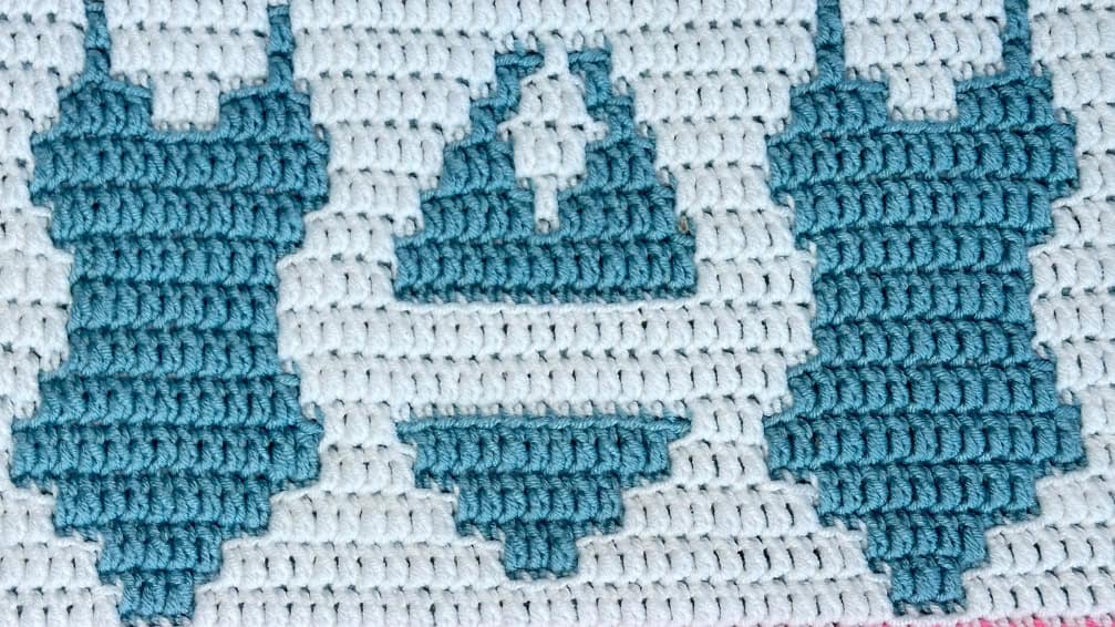 Close-up of a blue and white crochet blanket strip with swimsuit motifs