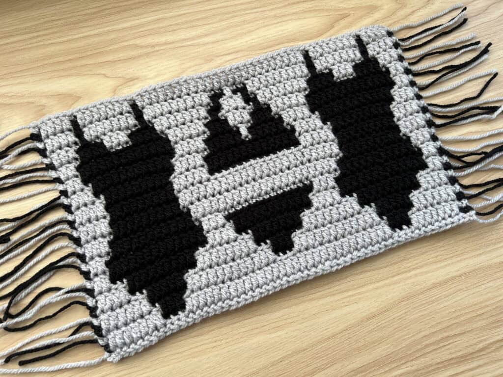 Black mosaic crochet swim suits design on a gray backdrop, laying on a wooden surface.