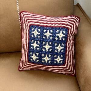 Handmade patriotic crochet pillow with stars and stripes design on a beige couch.