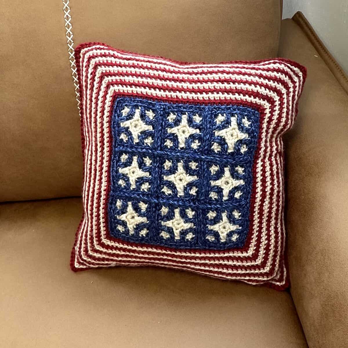 Handmade patriotic crochet pillow with stars and stripes design on a beige couch.