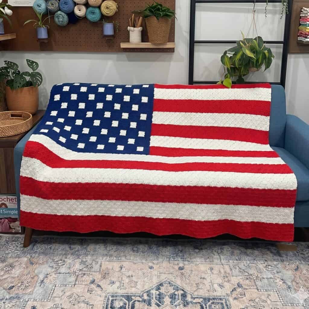 American flag c2c crochet blanket draped over a blue sofa in a cozy room.