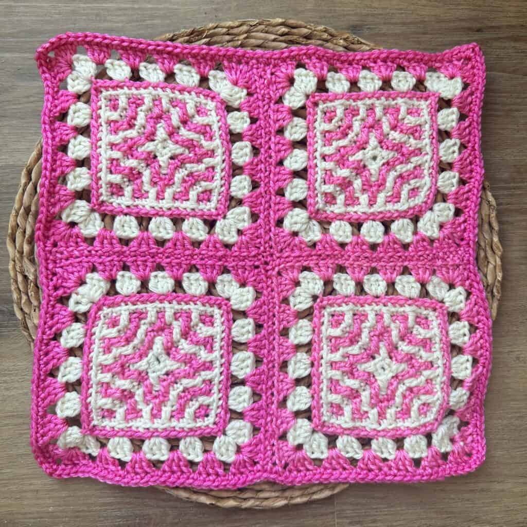Pink and white crocheted granny square blanket with intricate geometric patterns, displayed on a wov.