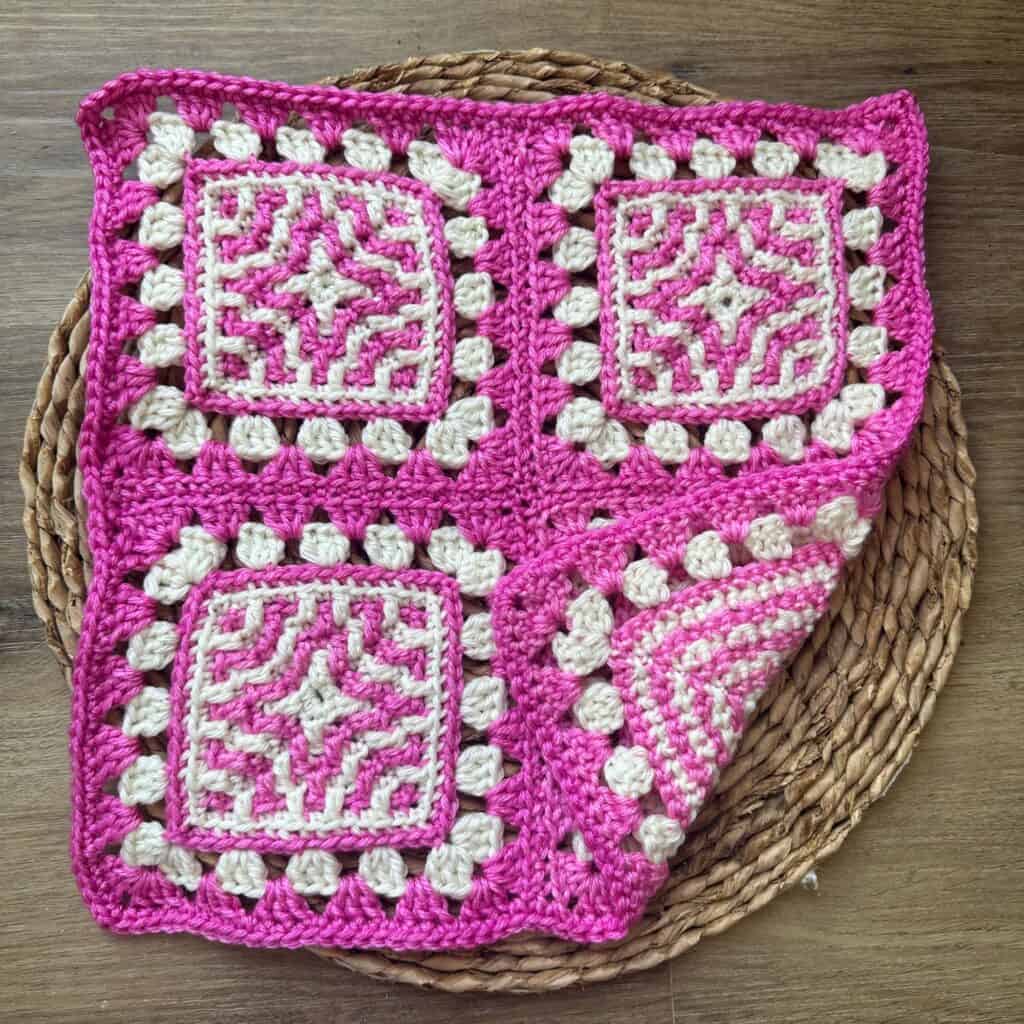Bright pink and white crocheted granny square blanket with intricate patterns, displayed on a woven.