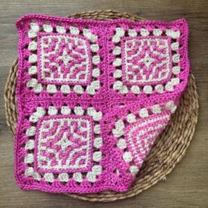 Bright pink and white crocheted granny square blanket with intricate patterns, displayed on a woven.