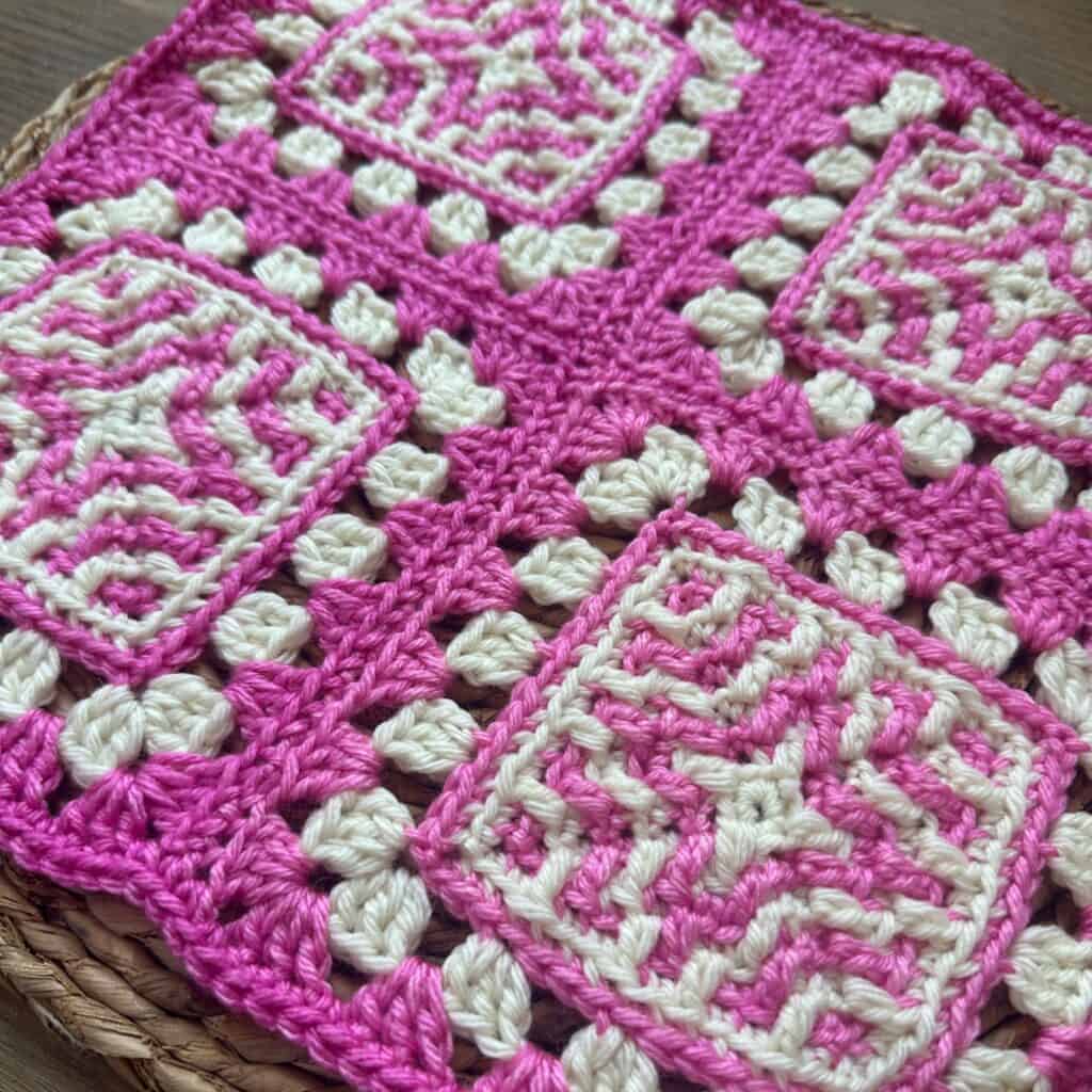 Bright pink and white crocheted blanket with intricate geometric patterns and textured details, show.