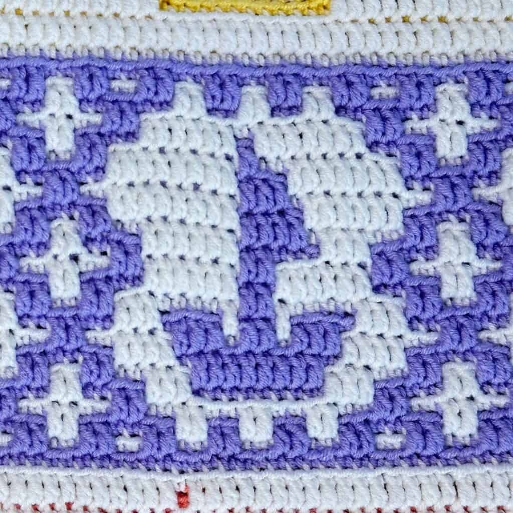 Close-up of a mosaic crochet sailboat pattern in white and purple yarn, designed by Joanna Robinson.