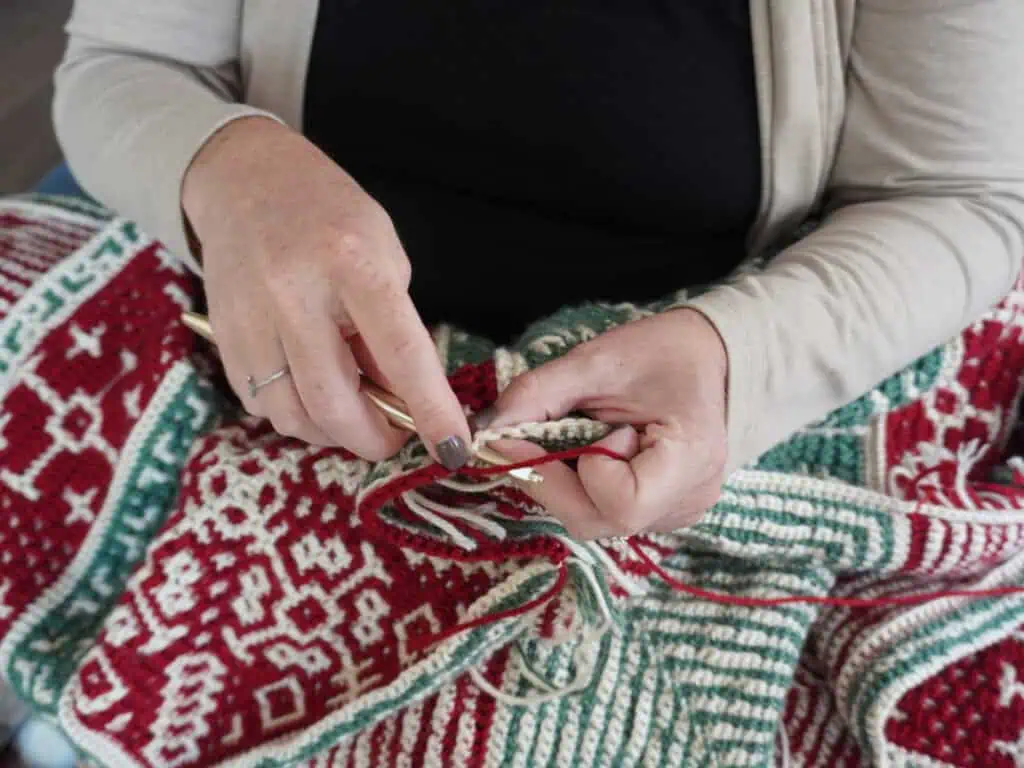 Close-up of person knitting a colorful holiday sweater with red, green, and white patterns.