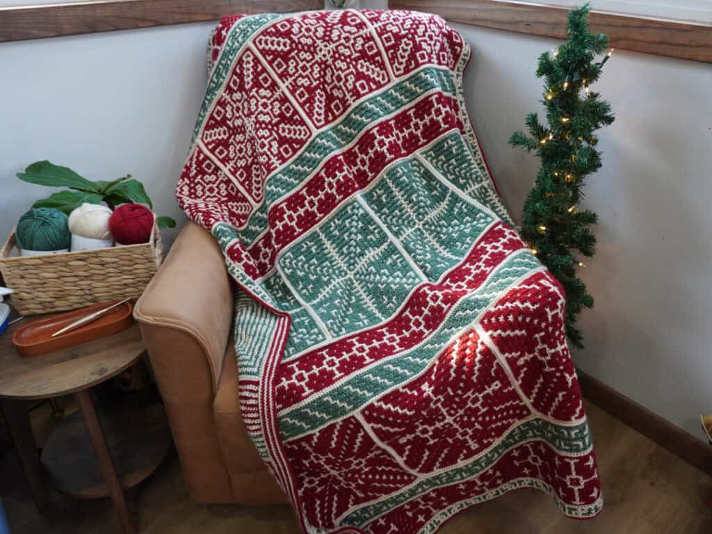 Cozy Christmas blanket with red, green, and white patterns on a beige armchair.