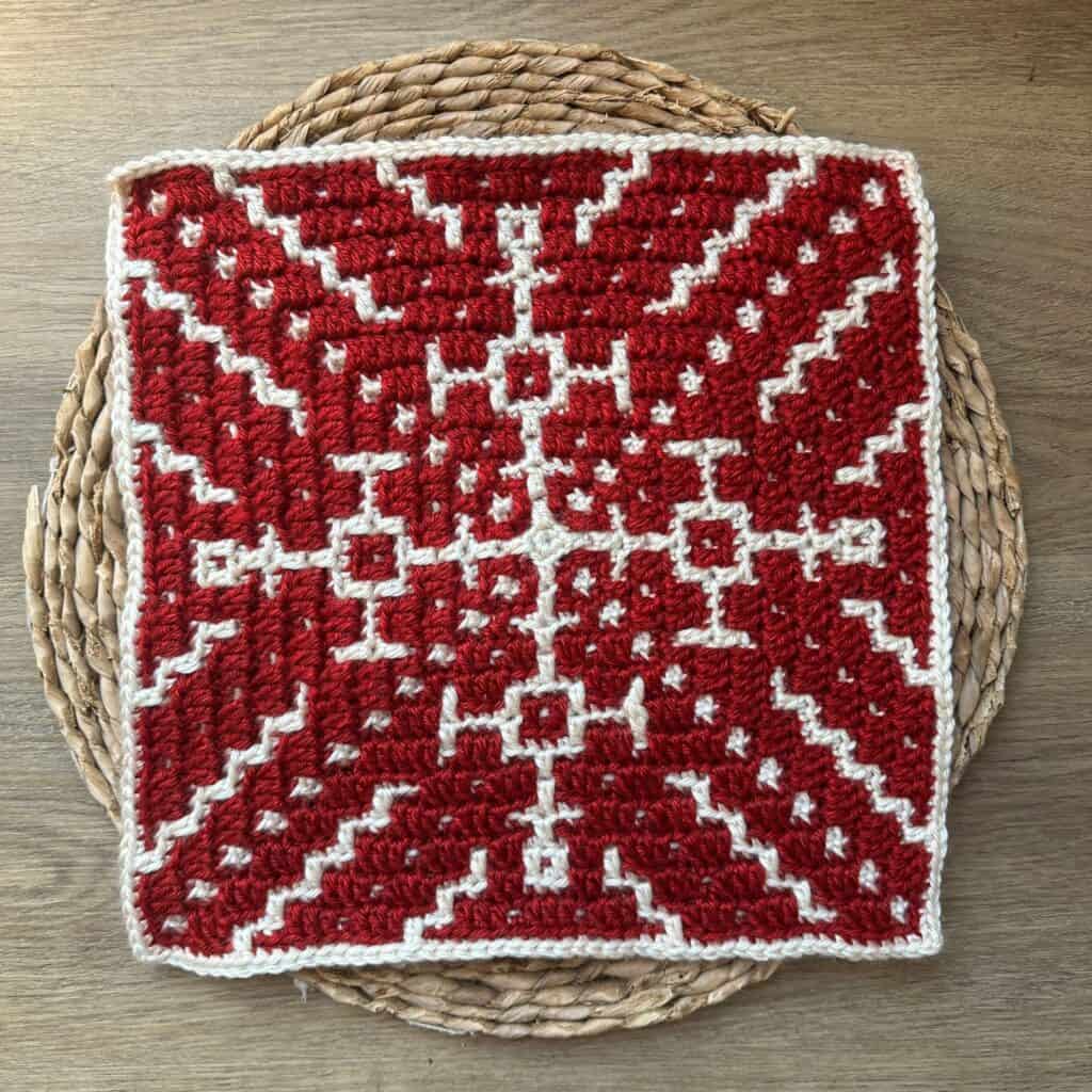 Crochet snowflake blanket with red and white pattern on woven placemat.