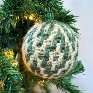 Crochet Christmas ornament with green and cream argyle pattern hanging on a decorated tree.