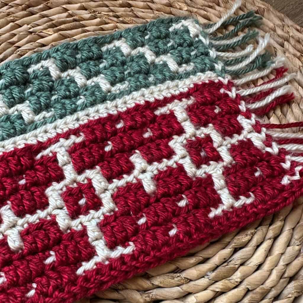 Crochet snowflake blanket with red, white, and green yarns on woven surface.