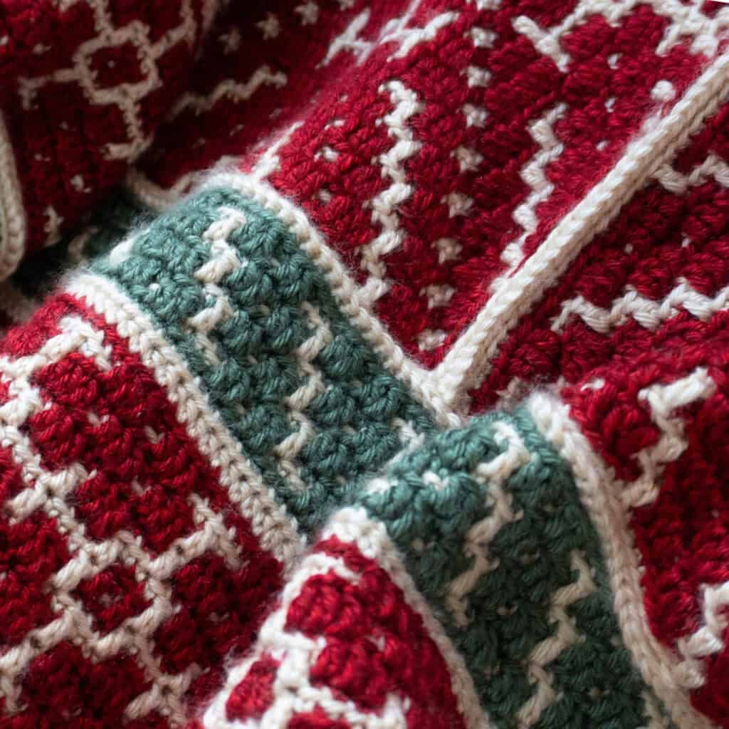 Close-up of a red, white, and green crochet blanket with intricate patterns.