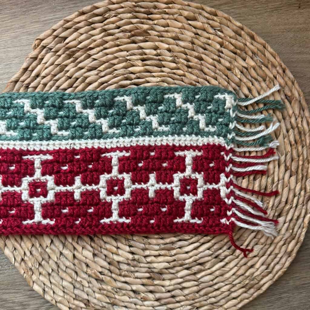 Crochet blanket with winter mosaic strip pattern on woven placemat.