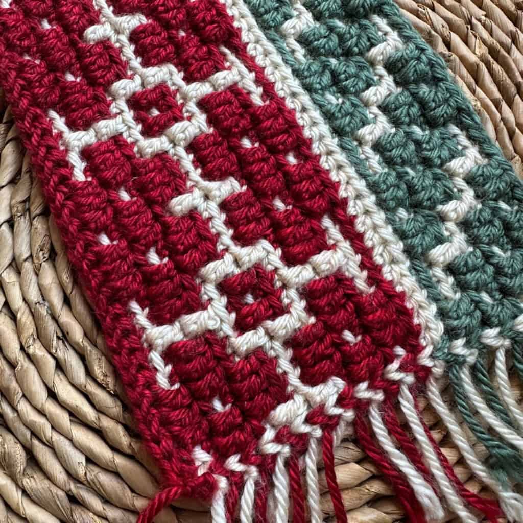 Close-up of a colorful crochet blanket with red, green, and beige yarns on a woven surface.