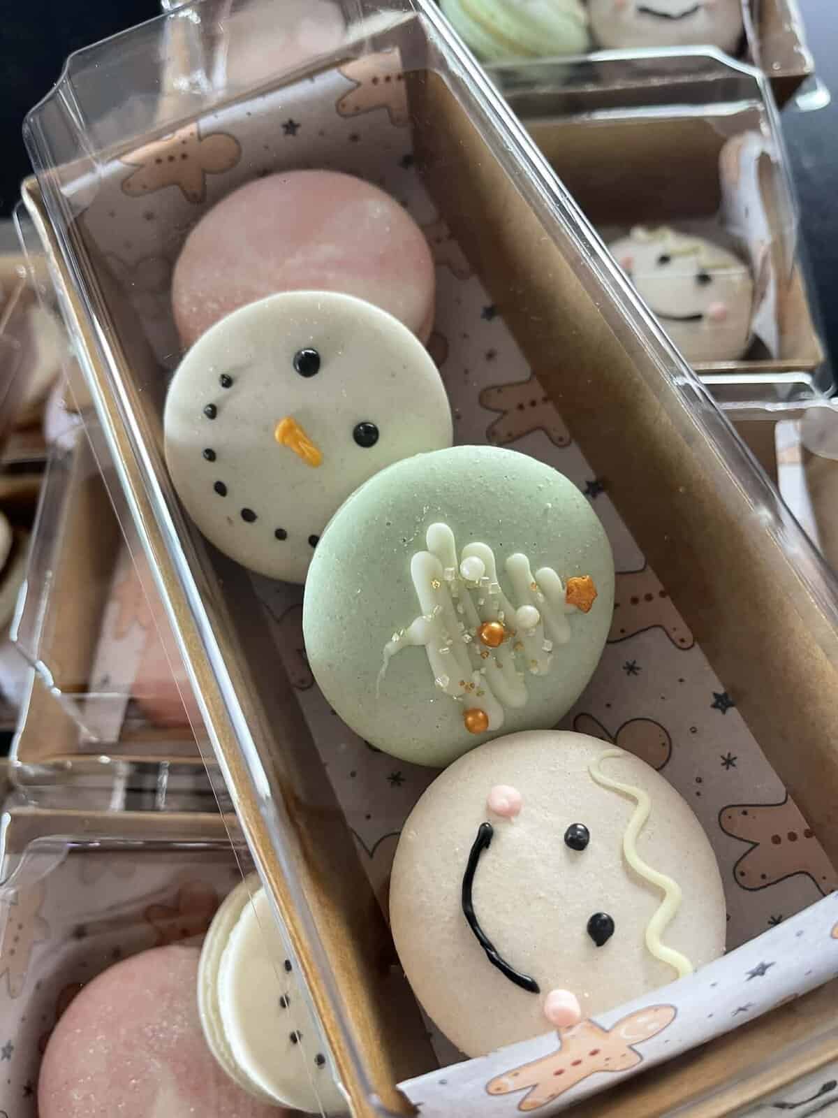Delicious holiday-themed macarons with snowman face, smiley, and festive decorations, perfect for Christmas treats.