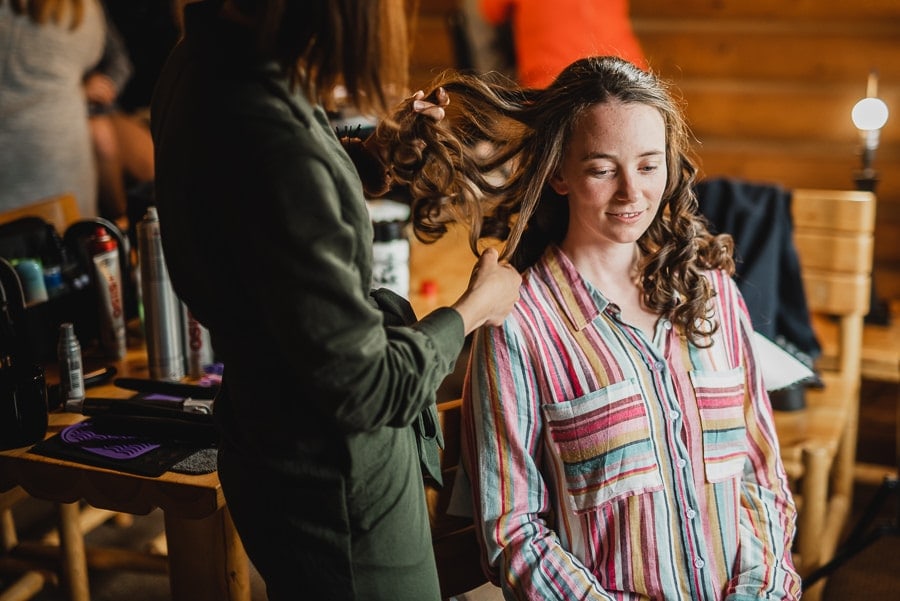 A person in a striped shirt sits and smiles while a stylist in casual clothing styles their hair, getting ready for Cooper Spur wedding photos.