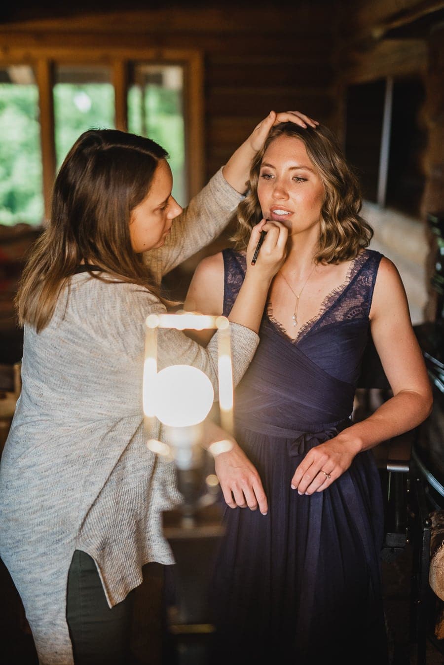 A woman in a navy dress is getting her makeup done in a well-lit room.