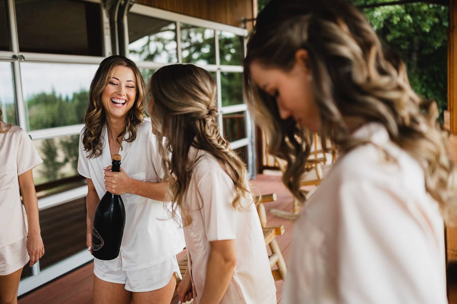 Women in matching outfits smile and hold a champagne bottle on the porch, celebrating at Scholls Valley Lodge.