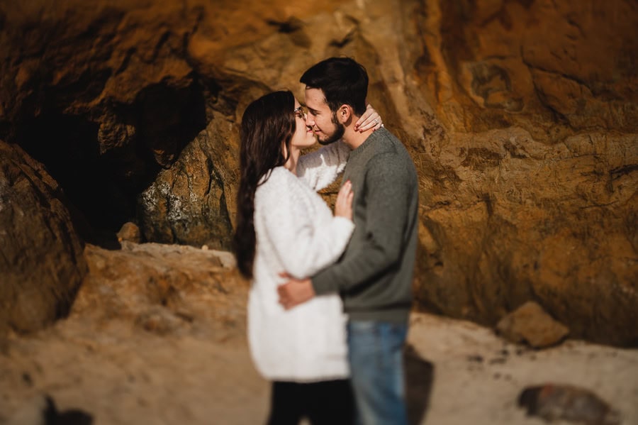 couple kissing romantically on beach with sandstone wall behind them