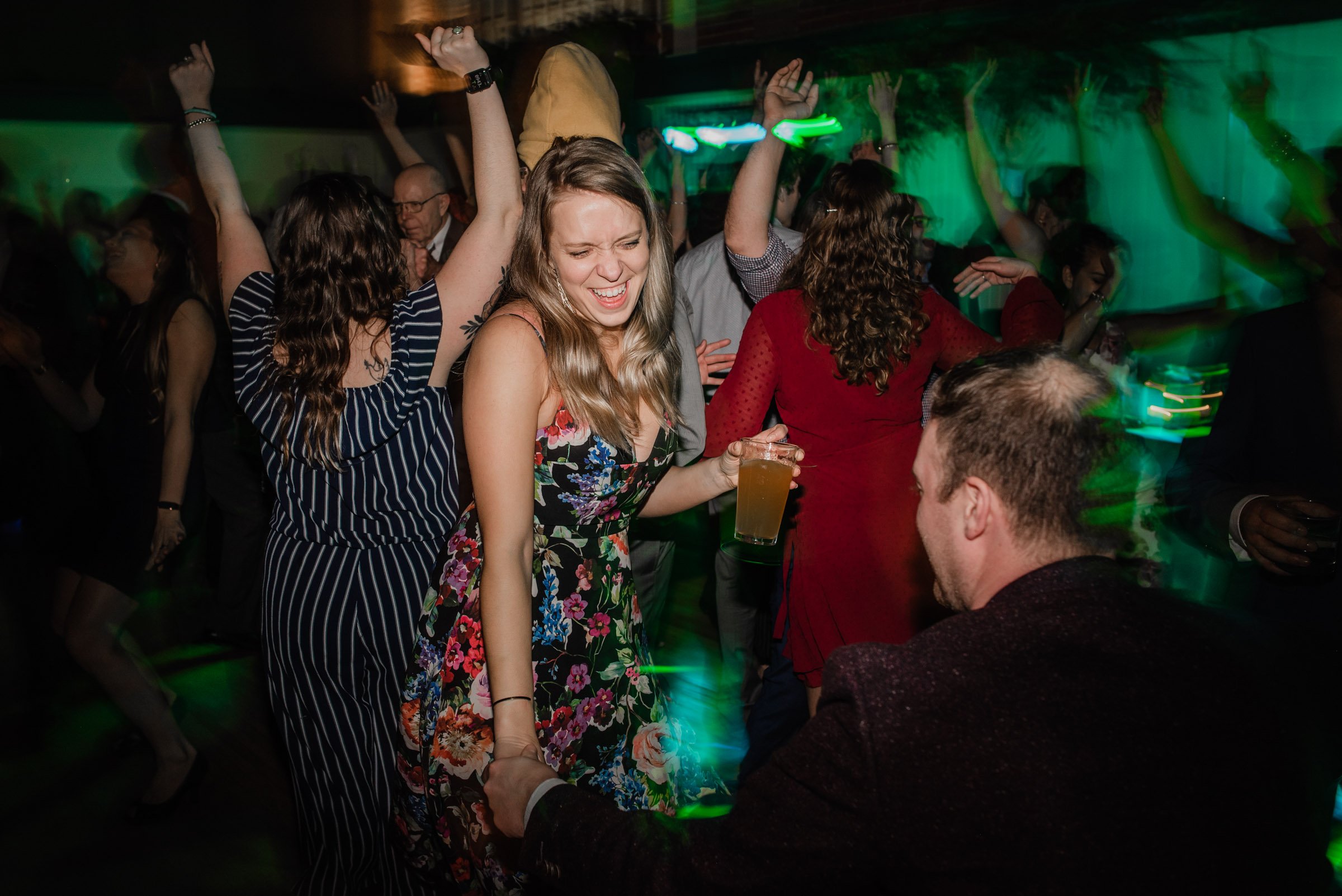 Guests danced energetically at the party, with a woman in a floral dress smiling and holding a drink. The lively atmosphere was reminiscent of wedding photos at The Evergreen.