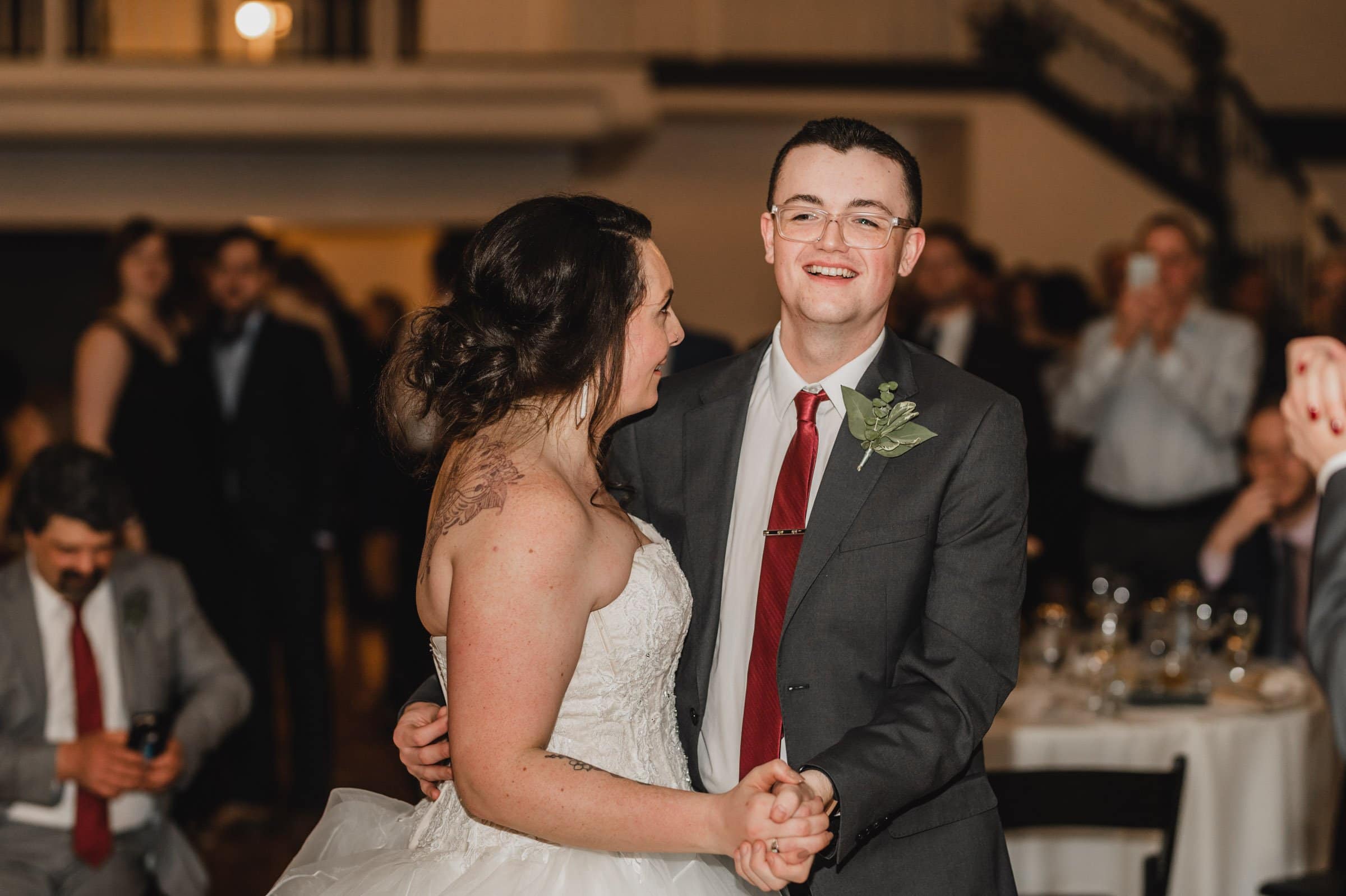 A couple in wedding attire joyfully dances at a reception, smiling and surrounded by guests, capturing the magic of their special day.