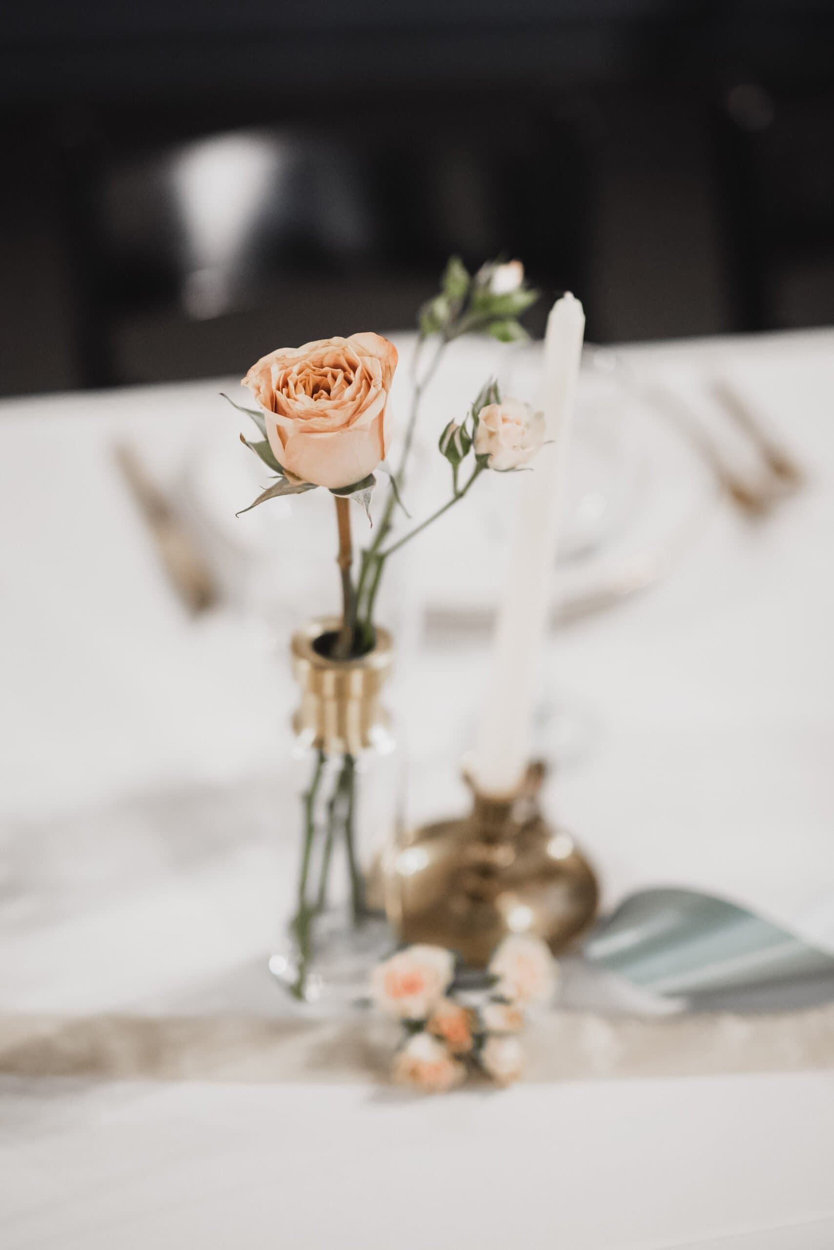 Peach roses in a glass vase and a white candle adorn a set dining table, creating an elegant ambiance perfect for wedding photos at The Evergreen.