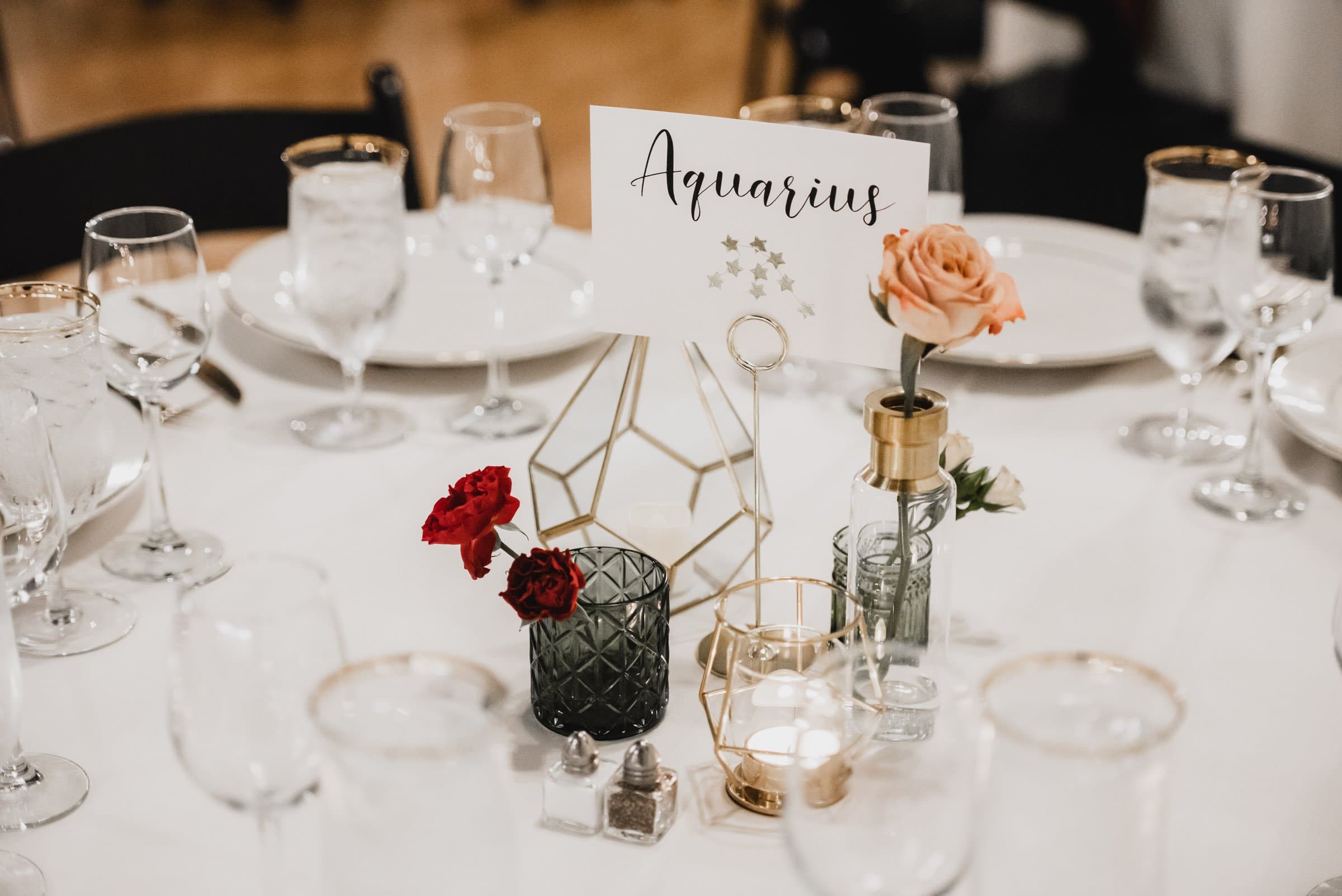 Elegant table setting featuring flowers and a card labeled Aquarius among glassware and geometric decor, perfect for wedding photos at The Evergreen.
