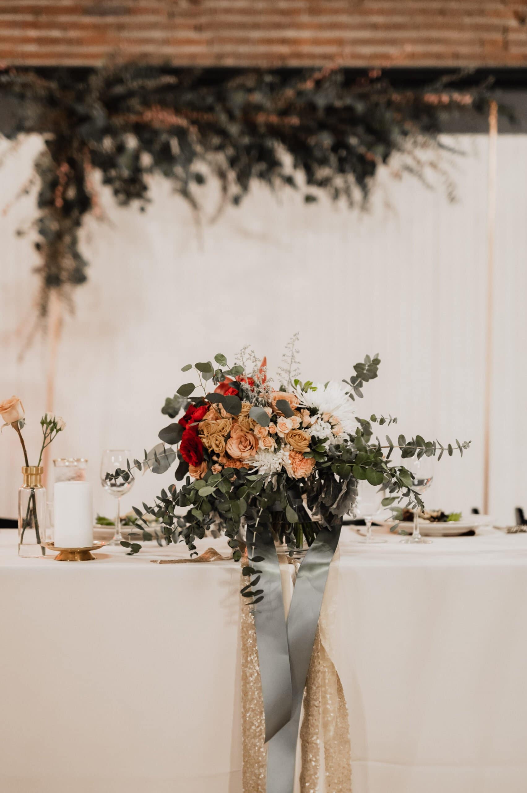 The elegant wedding table features a stunning floral centerpiece of red, white, and gold blooms on a pristine white tablecloth, perfect for capturing memorable wedding photos at The Evergreen.