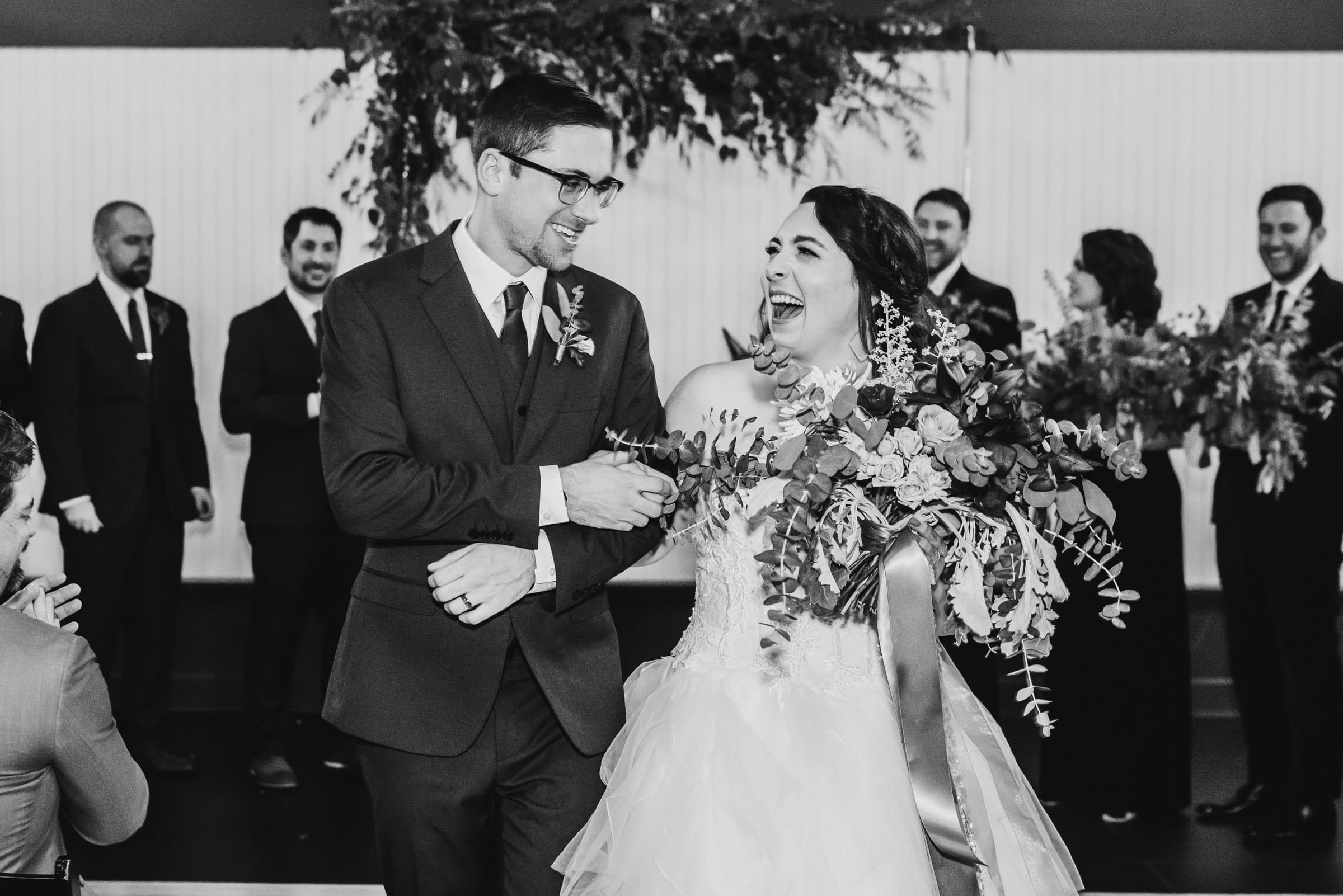 Bride and groom smile joyfully as they walk down the aisle, surrounded by their wedding party, capturing perfect wedding photos at The Evergreen.