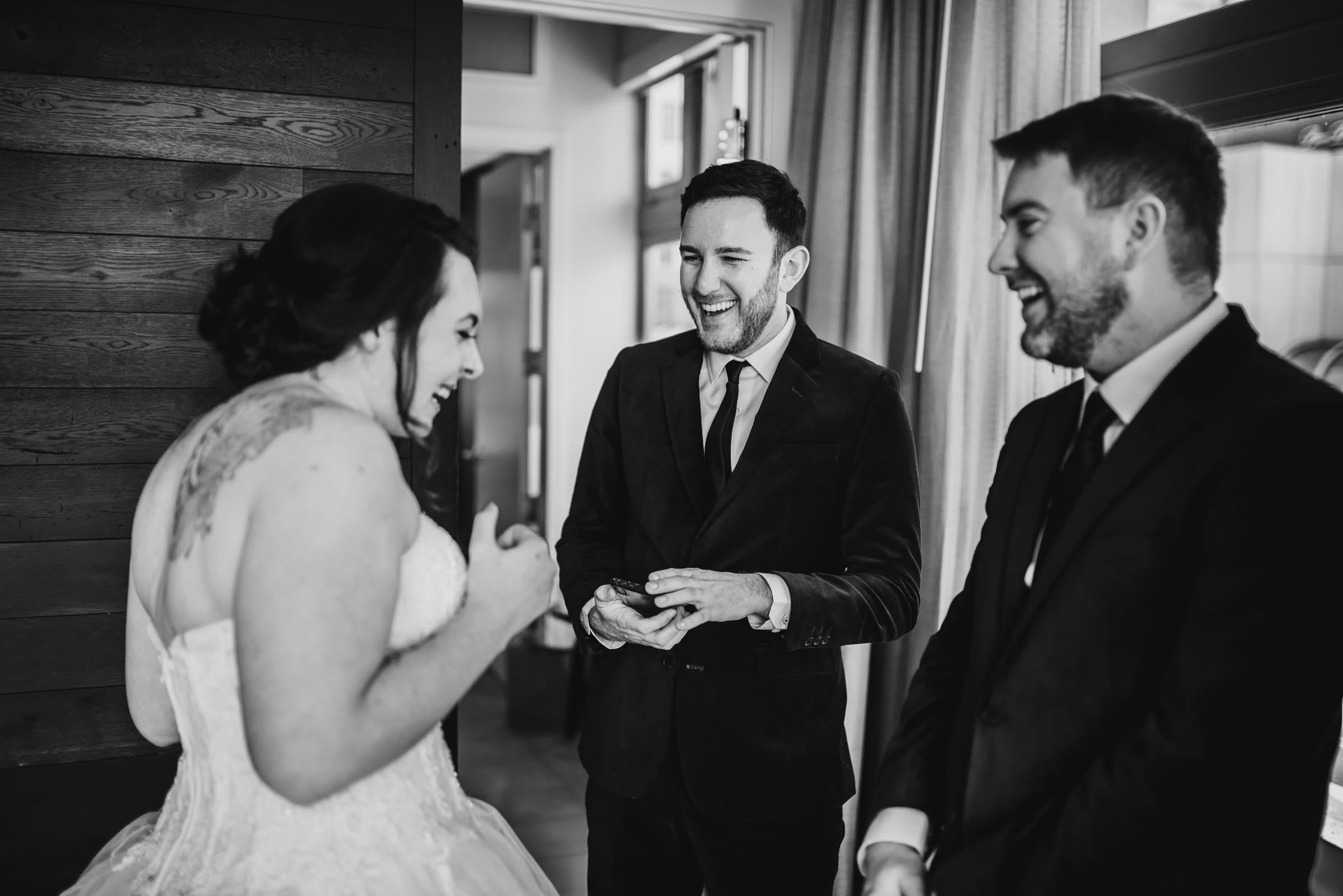 Bride and two groomsmen laughing together indoors at the Hi-Lo Hotel, dressed in formal attire.