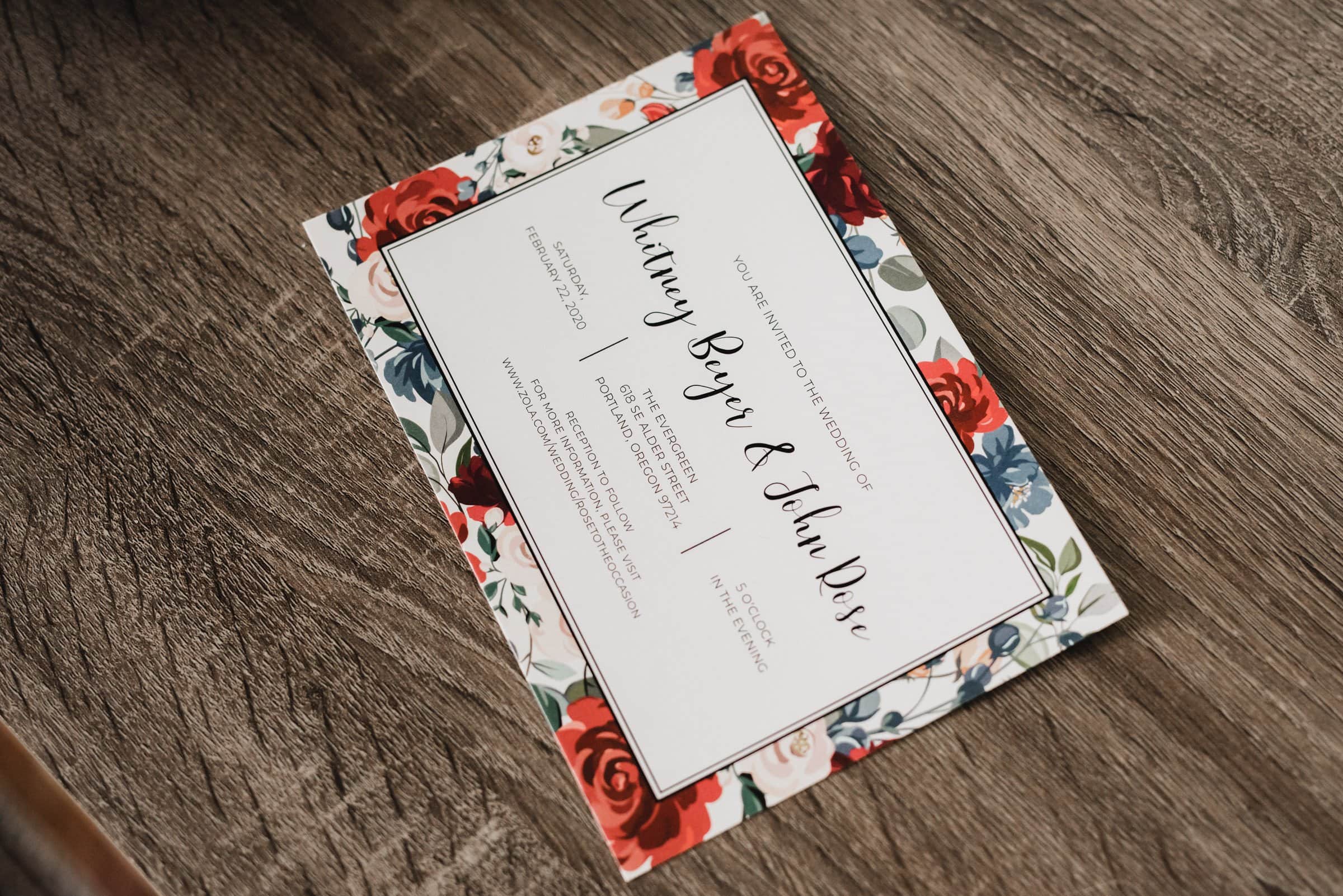 Wedding invitation featuring a floral border and cursive text rests elegantly on a wooden surface. Perfect for getting ready at a nearby apartment for a wedding at The Evergreen.